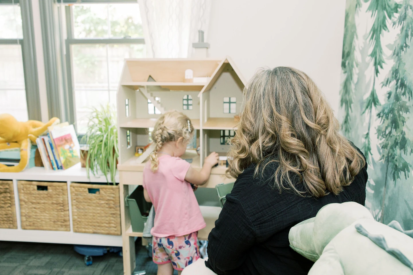 Therapist sitting on seat while child plays with a dollhouse during child play therapy session